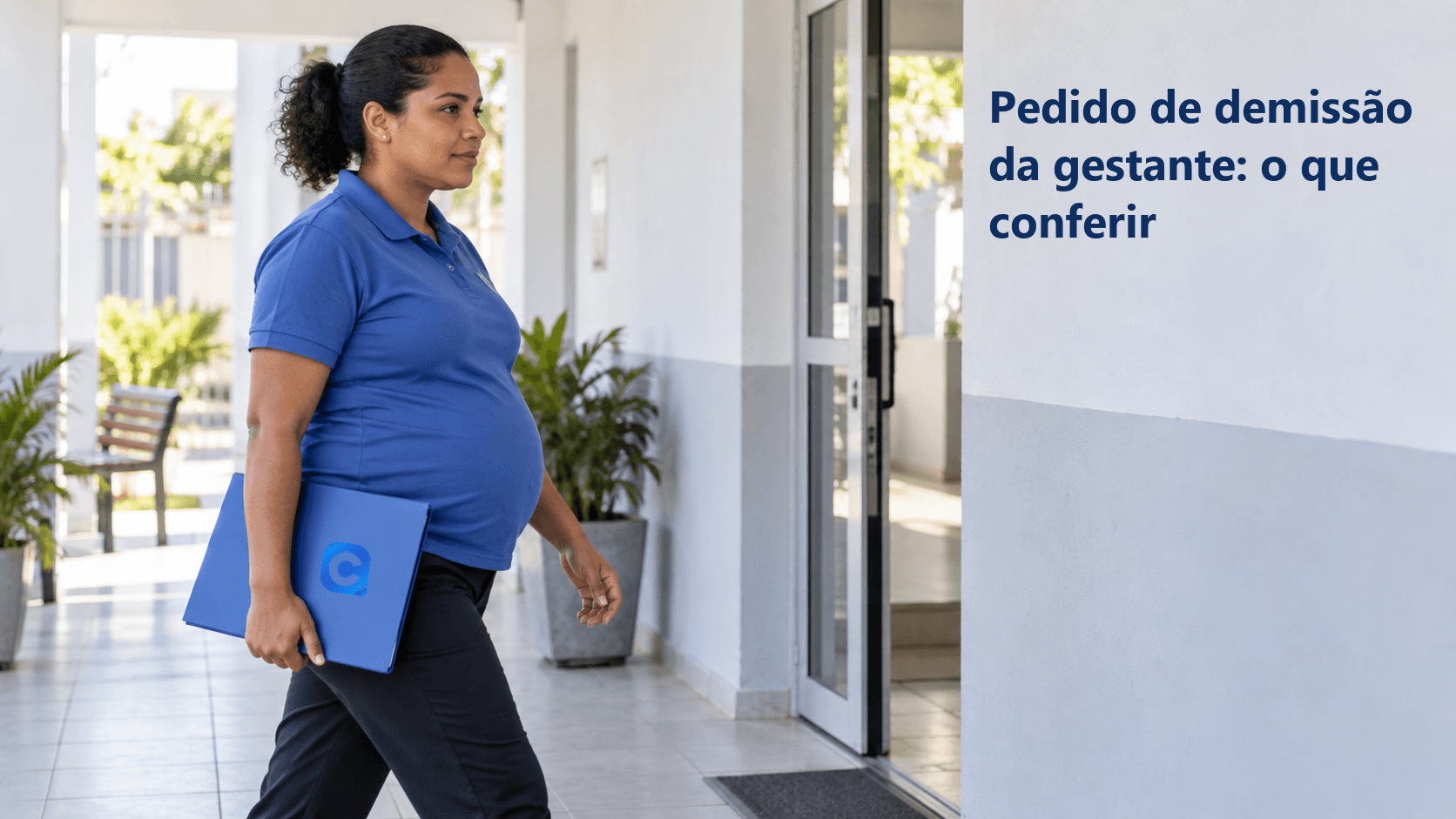 Trabalhadora grávida caminha por um corredor externo claro carregando uma pasta azul fechada.