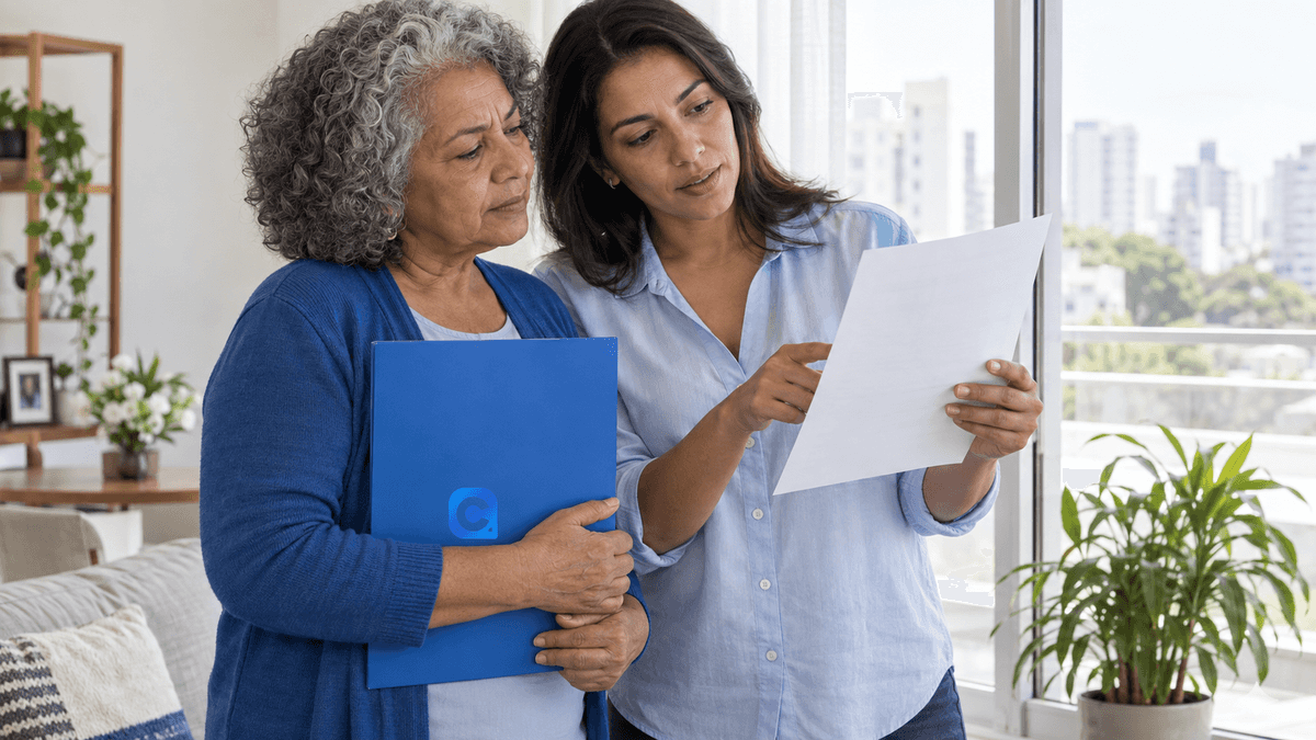 Duas mulheres maduras analisam com calma um demonstrativo de benefício em ambiente doméstico claro; símbolo Meu Consig discreto em pasta azul